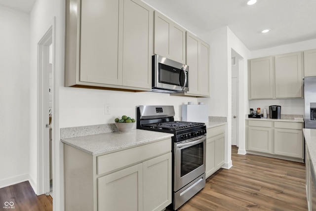 kitchen featuring baseboards, light stone counters, recessed lighting, appliances with stainless steel finishes, and wood finished floors