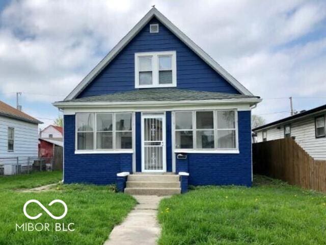 bungalow-style home with entry steps, a front lawn, and fence