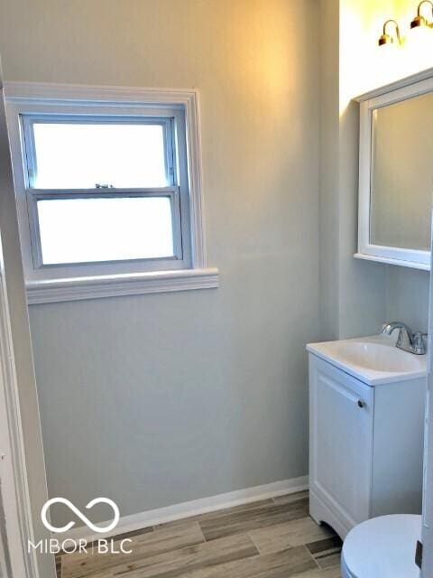 bathroom with toilet, vanity, baseboards, and wood finished floors