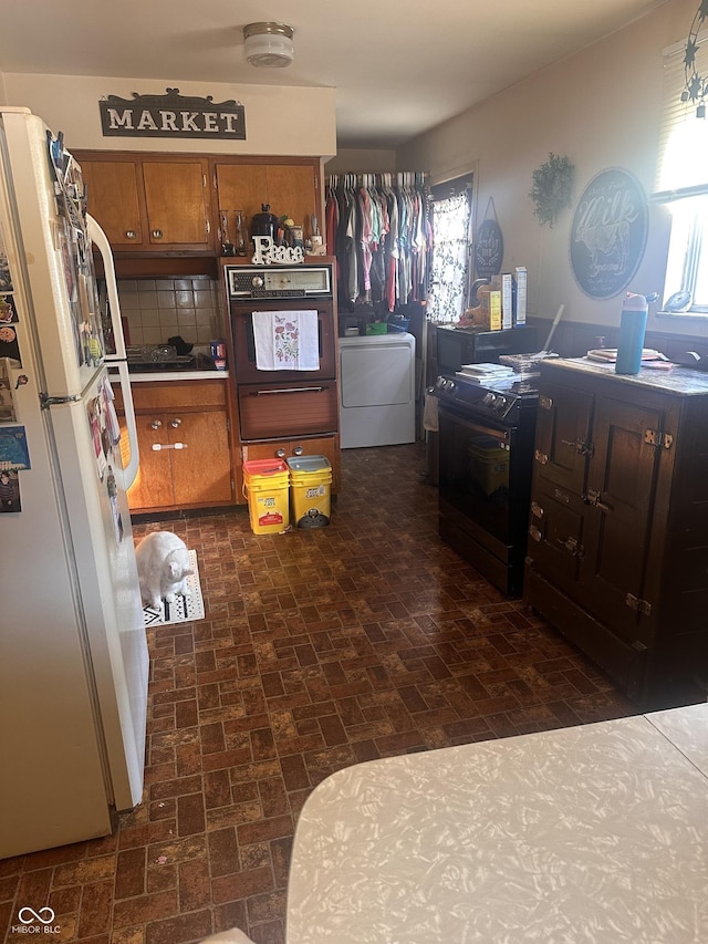 kitchen featuring oven, electric range, washer / clothes dryer, freestanding refrigerator, and brown cabinetry