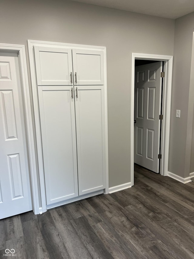 unfurnished bedroom with baseboards, a closet, and dark wood-style flooring