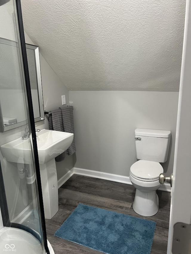 bathroom with baseboards, toilet, lofted ceiling, wood finished floors, and a textured ceiling