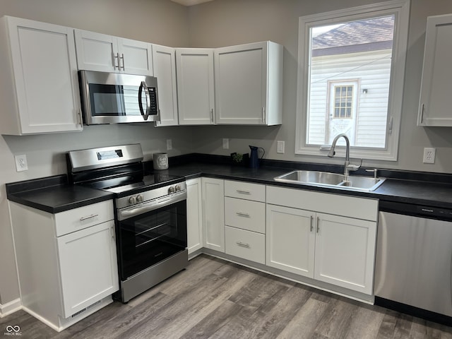 kitchen featuring dark countertops, a wealth of natural light, appliances with stainless steel finishes, wood finished floors, and a sink