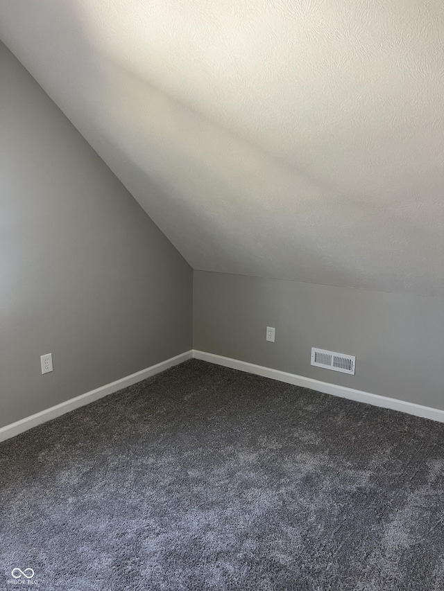 additional living space with visible vents, a textured ceiling, baseboards, and dark colored carpet