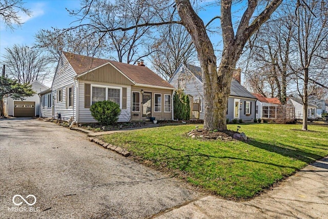 view of front of home with an outbuilding, aphalt driveway, a front yard, a garage, and a chimney