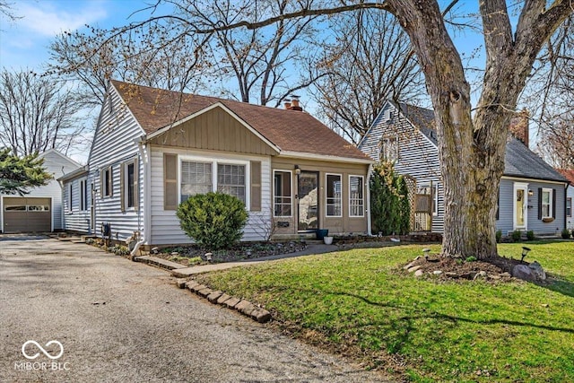 view of front of home with a detached garage, a front yard, a chimney, an outdoor structure, and driveway