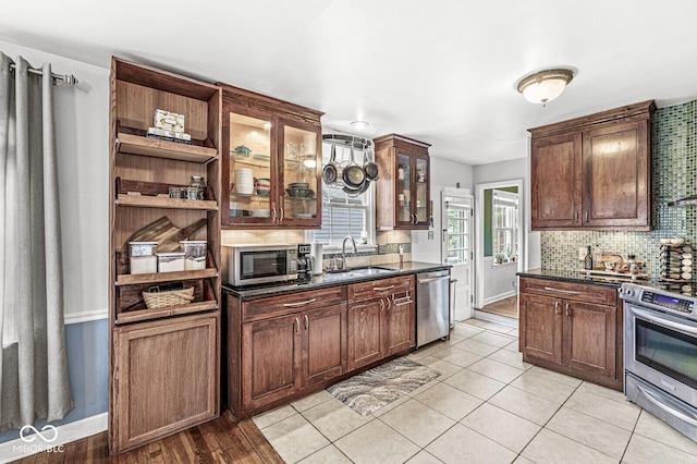 kitchen featuring open shelves, a sink, decorative backsplash, glass insert cabinets, and appliances with stainless steel finishes