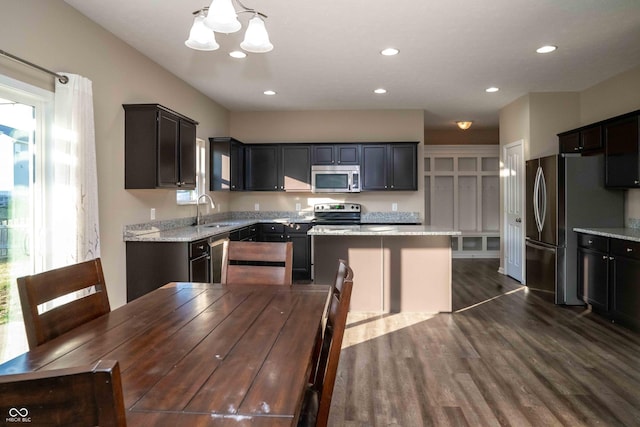 kitchen with light stone counters, an inviting chandelier, dark wood-style floors, stainless steel appliances, and a sink