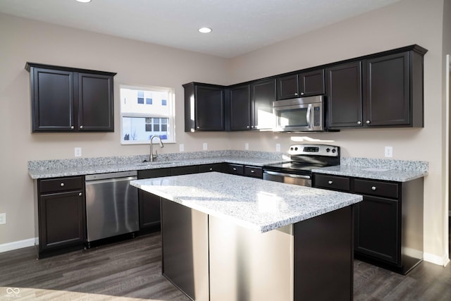 kitchen with a sink, light stone counters, a kitchen island, dark wood finished floors, and appliances with stainless steel finishes