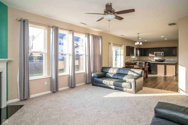 living area with light carpet, visible vents, ceiling fan with notable chandelier, and baseboards