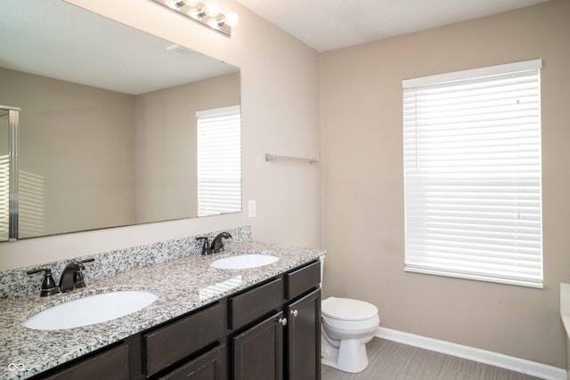 bathroom featuring double vanity, toilet, baseboards, and a sink