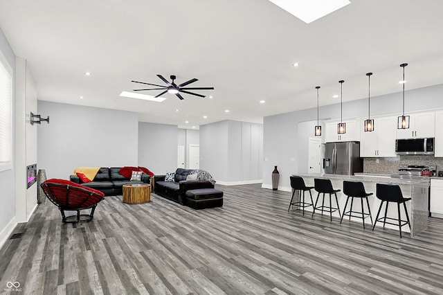 living room featuring recessed lighting, a skylight, baseboards, and wood finished floors