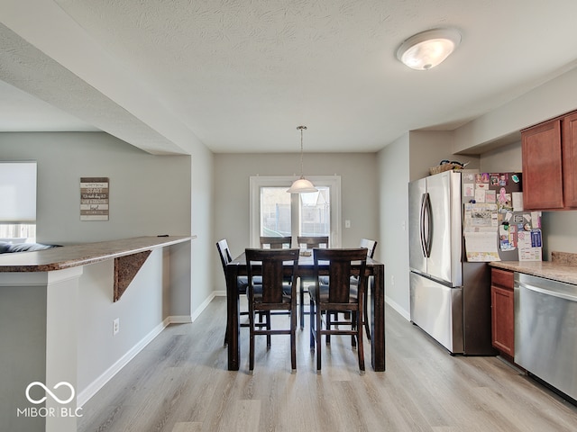 dining space with light wood finished floors, a textured ceiling, and baseboards