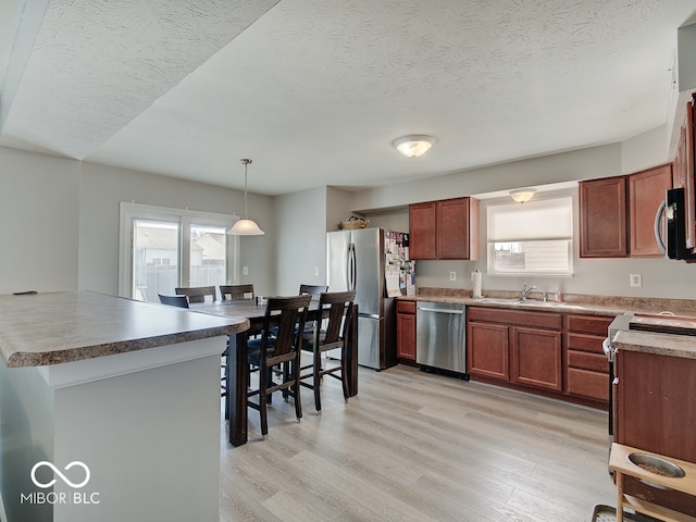 kitchen with light wood finished floors, pendant lighting, appliances with stainless steel finishes, a textured ceiling, and a sink