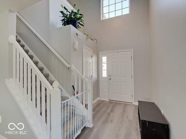 foyer entrance with stairs, baseboards, wood finished floors, and a towering ceiling