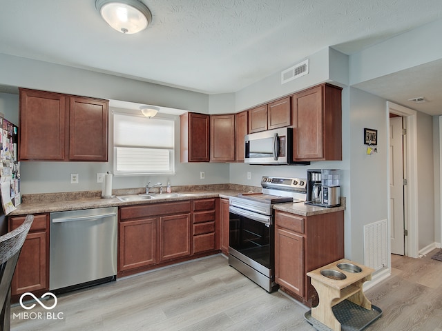 kitchen with a sink, stainless steel appliances, light wood-style floors, and visible vents