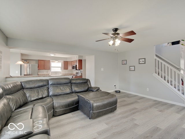 living room with stairs, a ceiling fan, light wood-type flooring, and baseboards