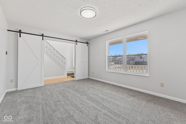 unfurnished room featuring baseboards, visible vents, a textured ceiling, a barn door, and carpet flooring