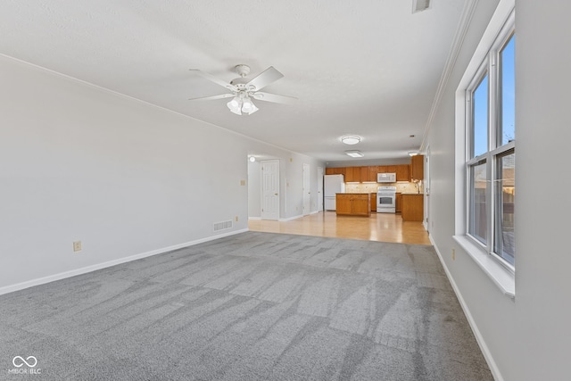 unfurnished living room with visible vents, baseboards, light colored carpet, ornamental molding, and a ceiling fan