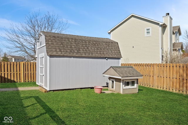 back of house with a shingled roof, a storage shed, a fenced backyard, a yard, and an outbuilding