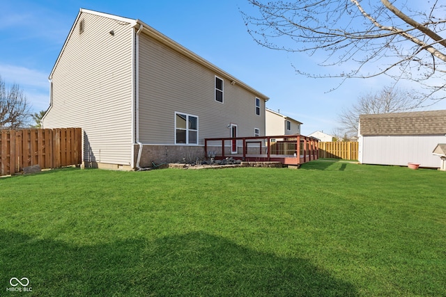 back of property featuring a yard, a deck, an outdoor structure, a fenced backyard, and a storage unit