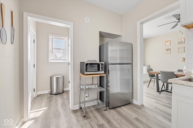 kitchen featuring baseboards, light wood-style flooring, appliances with stainless steel finishes, white cabinets, and a ceiling fan