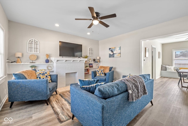 living area featuring a ceiling fan, wood finished floors, baseboards, recessed lighting, and a brick fireplace