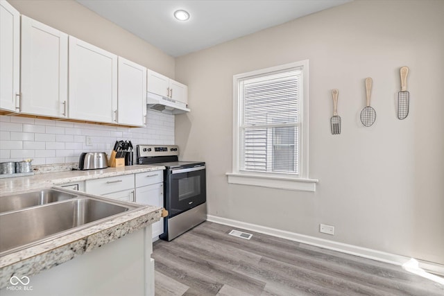 kitchen with stainless steel electric range oven, baseboards, white cabinets, under cabinet range hood, and backsplash