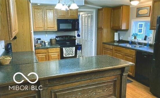 kitchen with dark countertops, a peninsula, an inviting chandelier, black appliances, and a sink