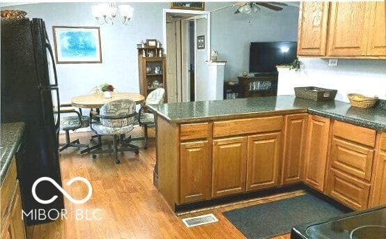 kitchen with wood finished floors, visible vents, a peninsula, freestanding refrigerator, and ceiling fan with notable chandelier