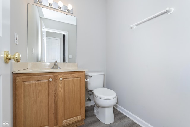 half bath with baseboards, toilet, wood finished floors, and vanity