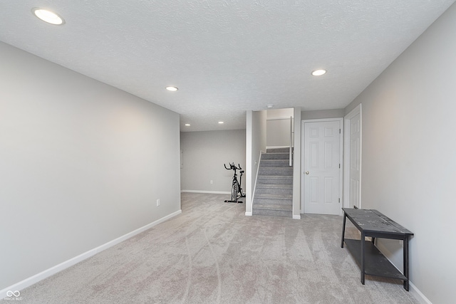 finished below grade area with light colored carpet, a textured ceiling, stairs, and baseboards