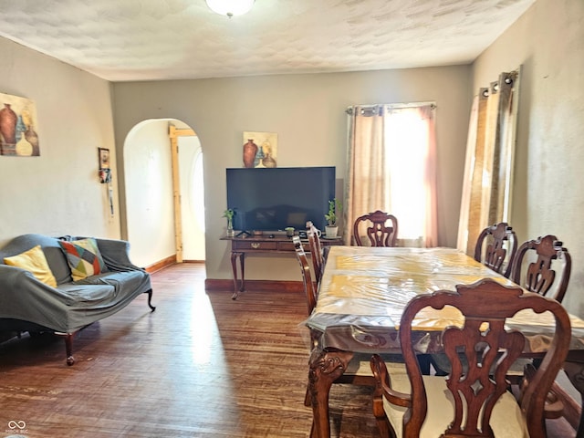 dining area featuring arched walkways, a textured ceiling, baseboards, and wood finished floors