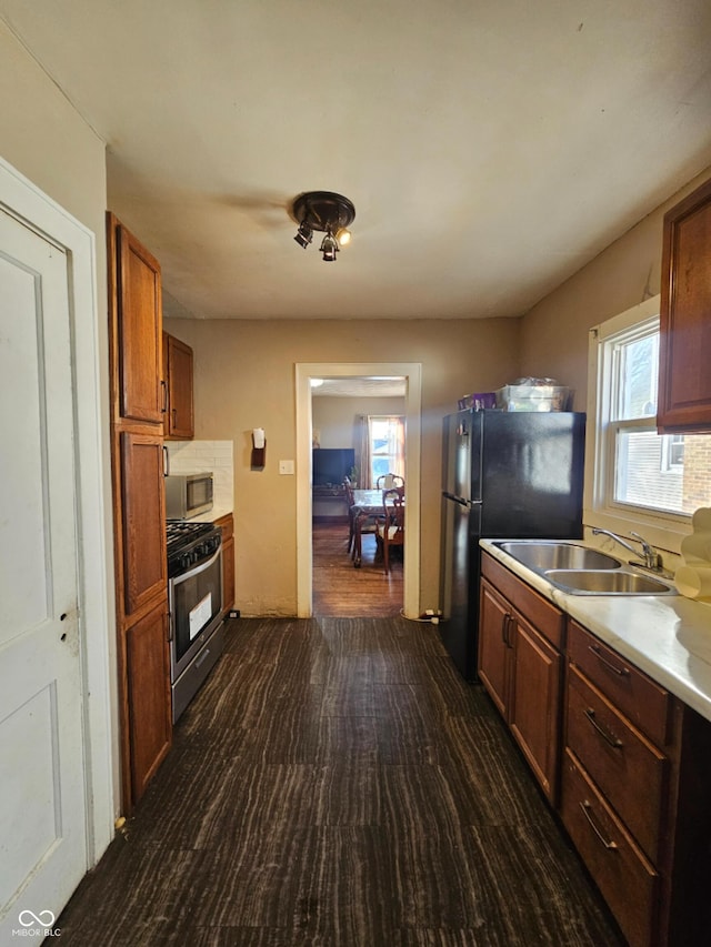 kitchen featuring dark wood finished floors, a sink, stainless steel appliances, light countertops, and brown cabinets