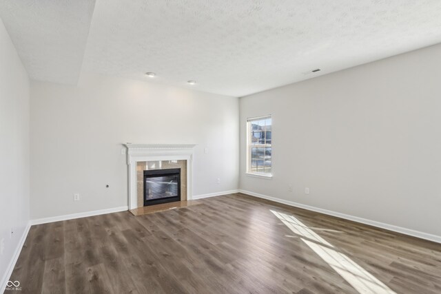 unfurnished living room featuring visible vents, a tiled fireplace, a textured ceiling, wood finished floors, and baseboards