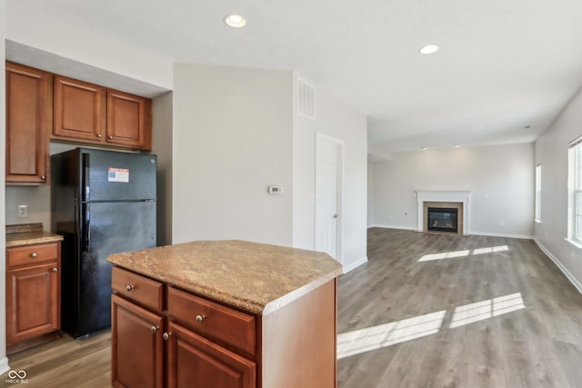 kitchen with a kitchen island, a glass covered fireplace, freestanding refrigerator, recessed lighting, and light wood-style floors