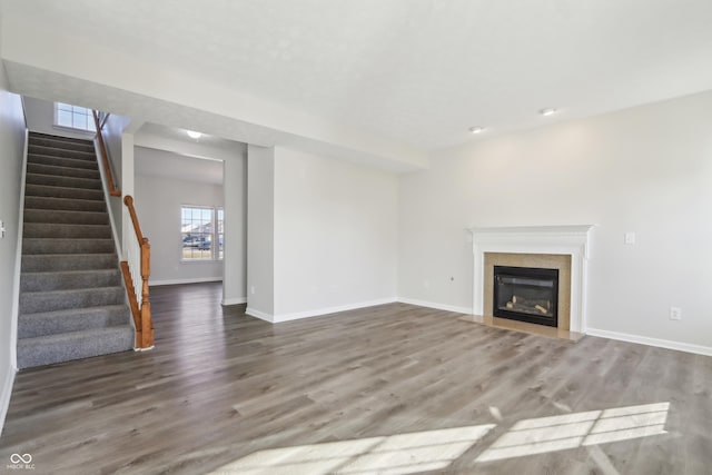 unfurnished living room with stairway, baseboards, a glass covered fireplace, and wood finished floors