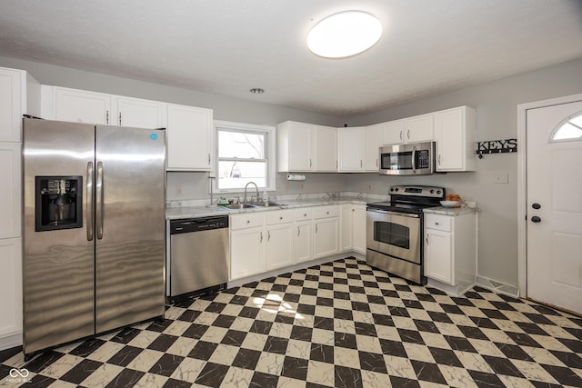 kitchen with light countertops, appliances with stainless steel finishes, tile patterned floors, white cabinets, and a sink