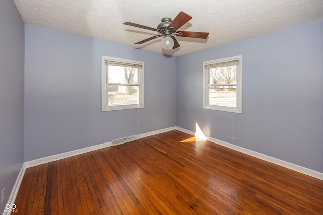 unfurnished room featuring a healthy amount of sunlight, visible vents, dark wood-style flooring, and baseboards