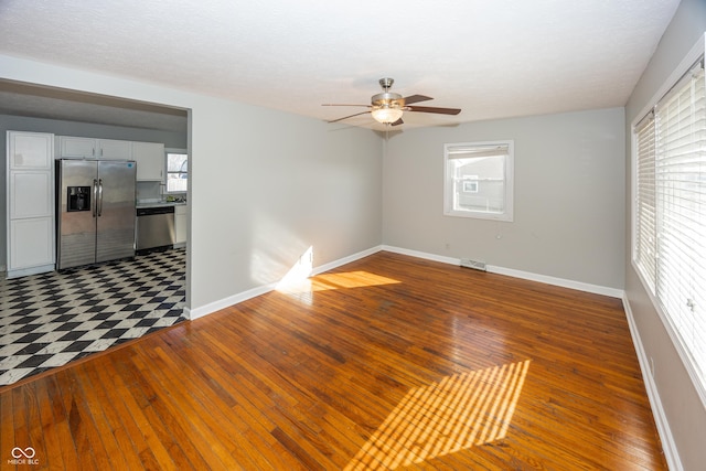 empty room with a ceiling fan, visible vents, wood-type flooring, and baseboards