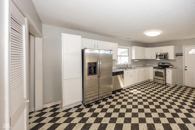 kitchen with a sink, a textured ceiling, white cabinetry, stainless steel appliances, and light countertops