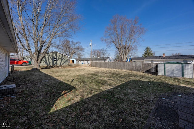 view of yard with fence, central AC, an outdoor structure, and a shed