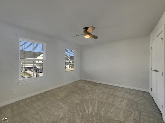 spare room with a ceiling fan, light colored carpet, and baseboards