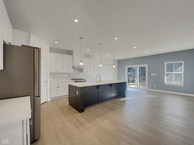 kitchen featuring light countertops, decorative backsplash, white cabinets, stainless steel appliances, and a kitchen island with sink