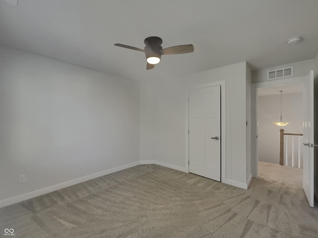 unfurnished bedroom with visible vents, light colored carpet, baseboards, and ceiling fan