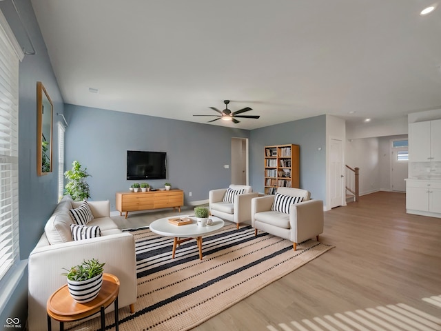 living area featuring stairway, light wood-style flooring, baseboards, and ceiling fan