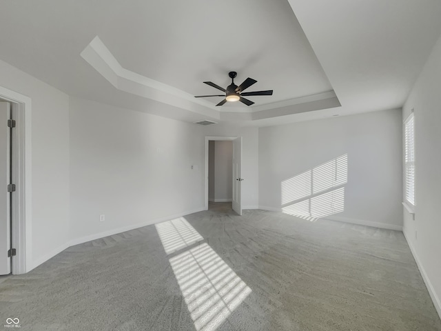 empty room with a tray ceiling, light carpet, baseboards, and visible vents