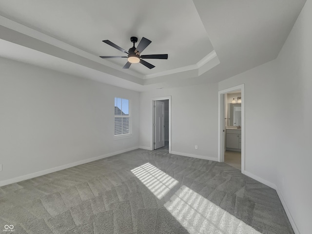 unfurnished bedroom with a raised ceiling, a ceiling fan, ensuite bath, carpet flooring, and baseboards