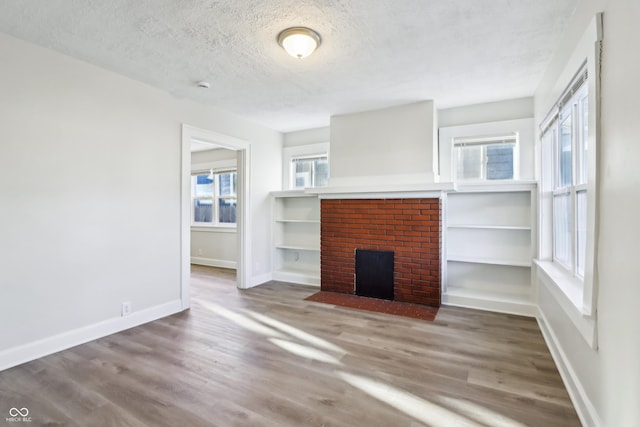 unfurnished living room with a fireplace, wood finished floors, baseboards, and a textured ceiling