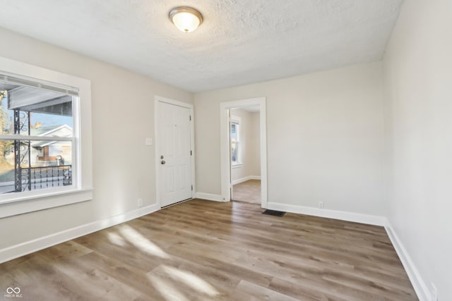 spare room featuring a healthy amount of sunlight, a textured ceiling, baseboards, and wood finished floors